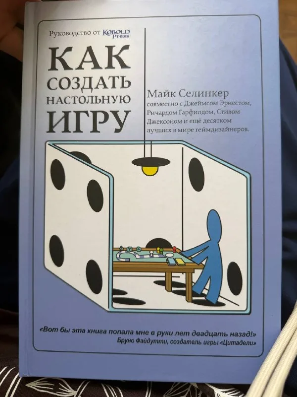 Обложка книги «Как создать настольную игру» с иллюстрацией человечка за игровым столом внутри игрального кубика