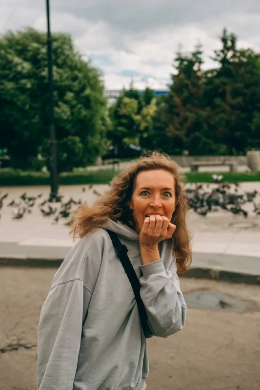Женщина с испуганным выражением лица на фоне стаи голубей в городском парке